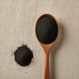Activated Charcoal Powder (Activated carbon) | Create a luxurious, photorealistic product photograph featuring the original product naturally arranged in an elegant handcrafted wooden spoon on a soft, finely