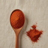 Annatto Seed Powder (Bixa Orellana) | Create a luxurious, photorealistic product photograph featuring the original product naturally arranged in an elegant handcrafted wooden spoon on a soft, finely