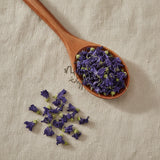 Blue Malva Flowers Whole (Malva Sylvestris) | Create a luxurious, photorealistic product photograph featuring the original product naturally arranged in an elegant handcrafted wooden spoon on a soft, finely