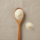Bovine Colostrum Powder (Bos Taurus) | Create a luxurious, photorealistic product photograph featuring the original product naturally arranged in an elegant handcrafted wooden spoon on a soft, finely