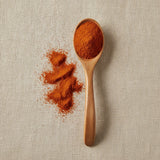 Cayenne Pepper Ground (30,000 HU) (Capsicum Annuum) | Create a luxurious, photorealistic product photograph featuring the original product naturally arranged in an elegant handcrafted wooden spoon on a soft, finely