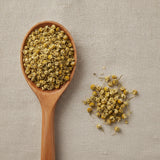 Chamomile Flowers Tea Bag Cut (Matricaria Recutita) | Create a luxurious, photorealistic product photograph featuring the original product naturally arranged in an elegant handcrafted wooden spoon on a soft, finely