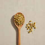 Chamomile Flowers Whole (Matricaria Camomilla) | Create a luxurious, photorealistic product photograph featuring the original product naturally arranged in an elegant handcrafted wooden spoon on a soft, finely