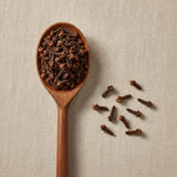 Cloves Whole (Syzygium Aromaticum) | Create a luxurious, photorealistic product photograph featuring the original product naturally arranged in an elegant handcrafted wooden spoon on a soft, finely