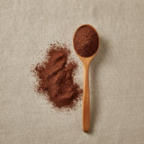 Guittard Cocoa Powder (Dutch Process) (Theobroma Cacao) | Create a luxurious, photorealistic product photograph featuring the original product naturally arranged in an elegant handcrafted wooden spoon on a soft, finely