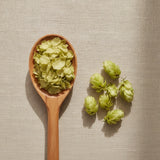 Hops Flowers Whole (Humulus Lupulus) | Create a luxurious, photorealistic product photograph featuring the original product naturally arranged in an elegant handcrafted wooden spoon on a soft, finely