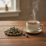 Jasmine Pearls Tea (Camellia Sinensis) | Can you show this tea outside of the bag and bowl, on a table next to a hot tea cup in a rustic home.