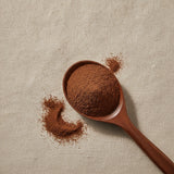 Kola Nut Powder (Cola Acuminate) | Create a luxurious, photorealistic product photograph featuring the original product naturally arranged in an elegant handcrafted wooden spoon on a soft, finely
