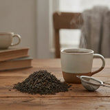 Oolong Tea (Camellia Sinensis) | Can you show this tea outside of the bag and bowl, on a table next to a hot tea cup in a rustic home.