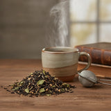 Raspberry Fruit Black Tea (Camellia Sinensis) | Can you show this tea outside of the bag and bowl, on a table next to a hot tea cup in a rustic home.