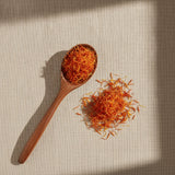 Safflower Petals (Carthamus Tinctorius) | Create a luxurious, photorealistic product photograph featuring the original product naturally arranged in an elegant handcrafted wooden spoon on a soft, finely