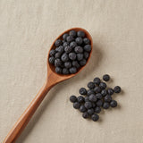 Sloe Berries Whole (Prunus Spinosa) | Create a luxurious, photorealistic product photograph featuring the original product naturally arranged in an elegant handcrafted wooden spoon on a soft, finely