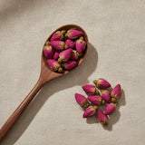 Wild Rose Buds (Rosa Rugosa) | Create a luxurious, photorealistic product photograph featuring the original product naturally arranged in an elegant handcrafted wooden spoon on a soft, finely
