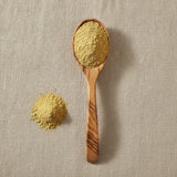 Yellow Mustard Seed Powder (Sinapis Alba) | Create a luxurious, photorealistic product photograph featuring the original product naturally arranged in an elegant handcrafted wooden spoon on a soft, finely